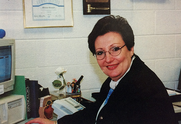 Color portrait of Principal Brower from our 1995 to 1996 yearbook. She is pictured at her desk where she is working on a computer. 