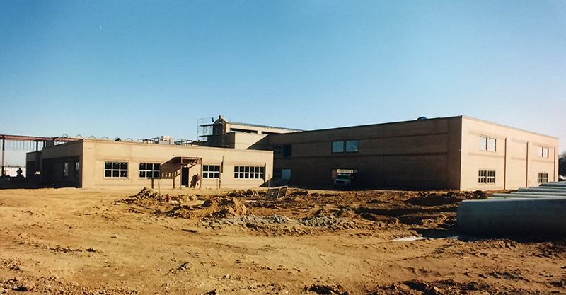 Exterior view of Lane Elementary School during construction taken on January 4, 1995. The photograph was taken from Beulah Street looking northeast toward the school. The brick façade is in place, but the main entrance still has bare steel framing above it. Scaffolding can be seen in the distance on the opposite side of the building. The school grounds are still bare earth, and large concrete pipes are lined up in a row on the right side of the photograph. 