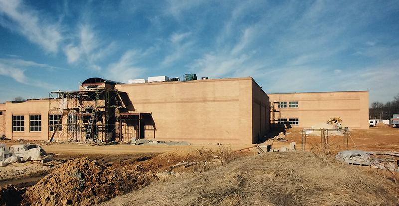 Exterior view of Lane Elementary School during construction taken on February 3, 1995. The brick façade is in place around the building. Scaffolding is in place over one of the entrances. The grounds are bare earth, with dirt piled in large heaps.  